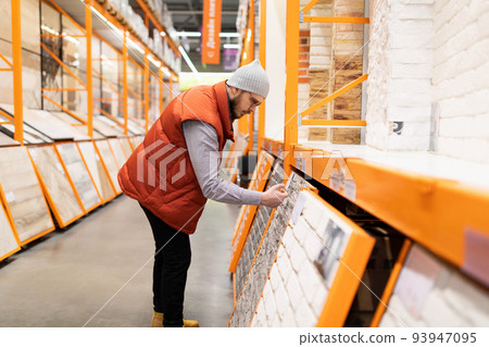 customer in a construction hypermarket next to a rack with ceramic tiles and artificial stone customer in a construction hypermarket next to a rack with ceramic tiles and artificial stone 93947095