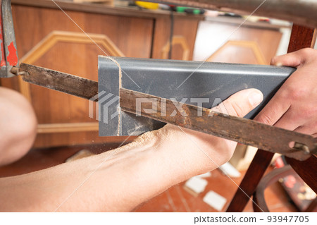 Trimming a wooden plinth with a manual jigsaw. 93947705