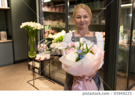 an employee of a florist's shop demonstrates a ready-made bouquet to a customer 93949225