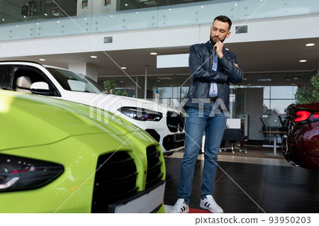 a young man chooses a sports car for himself in a car dealership a young man chooses a sports car for himself in a car dealership 93950203