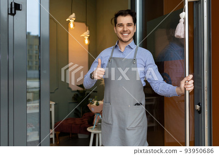 the owner of a cozy establishment kindly and cordially meets his clients on the threshold of the 93950686