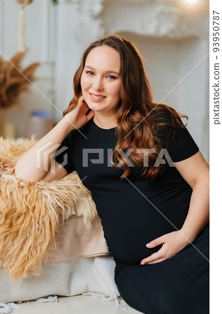 an attractive pregnant woman in a black dress by the bed of the house. 93950787