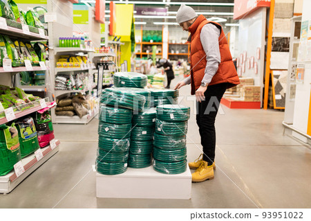 a man in a garden hypermarket is selected Come on a hose for watering work a man in a garden hypermarket is selected Come on a hose for watering work 93951022