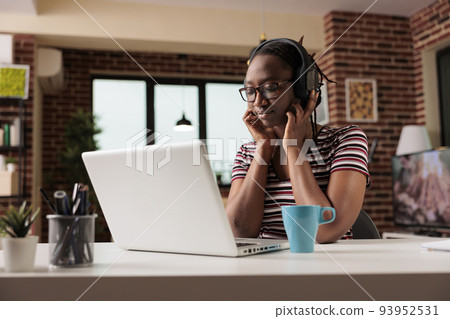 Young african american woman in wireless headphones watching movie online on streaming service on laptop, freelancer having break from work. Teenager leisure activity, home entertainment 93952531