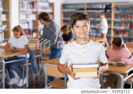 Boy with pile of books in library 93958712
