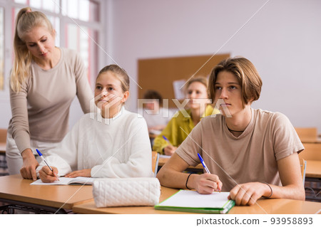 Teenage high school students studying in college with classmates, making notes of teacher lecture Teenage high school students studying in college with classmates, making notes of teacher lecture 93958893