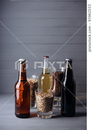 bottles with craft beer  and beer glasses with barley malt on a grey wooden background.  Ale or lager from pilsner malt.  homemade home-brewed beer. 93962033