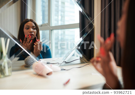 Black female entrepreneur sitting at vanity and applying liquid lipstick when getting ready for work Black female entrepreneur sitting at vanity and applying liquid lipstick when getting ready for work 93962721