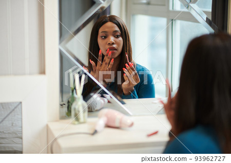 Businesswoman applying lipstick at her vanity when getting ready for meeting Businesswoman applying lipstick at her vanity when getting ready for meeting 93962727