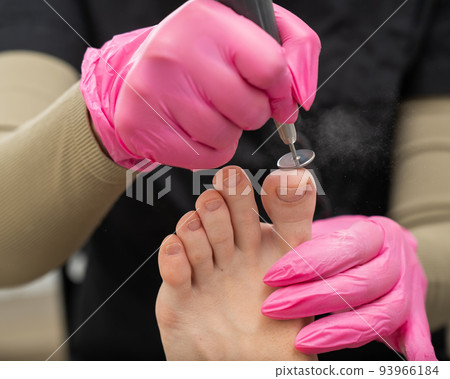 A pedicurist treats the toes of a client using a machine with an abrasive disc in a beauty salon. 93966184