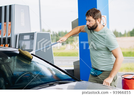 man washing windshield of car at gas station 93966855