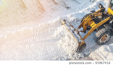 Big orange tractor removes snow from the road and clears the sidewalk Big orange tractor removes snow from the road and clears the sidewalk 93967418