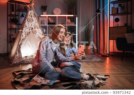 Beautiful cute sisters or friends sitting outside wigwam with smartphone. Beautiful cute sisters or friends sitting outside wigwam with smartphone. 93971342