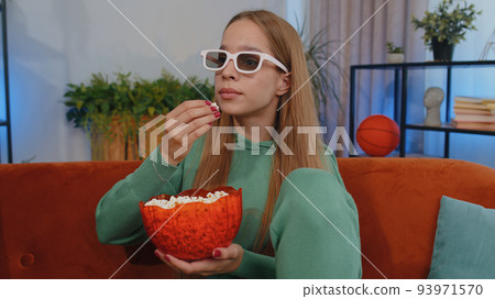 Girl sitting on couch eating popcorn and watching interesting TV serial, sport game online at home Girl sitting on couch eating popcorn and watching interesting TV serial, sport game online at home 93971570