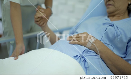 Asian young woman taking care of her mother who resting on the bed in hospital ward. Young woman talking to elder woman. 93971725