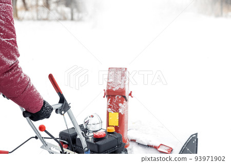 Closeup of portable red snow blower powered by gasoline in action. Man outdoor using snowblower machine after snowstorm for clearing, removing snow on snowy road. Snow removal, thrower assistant Closeup of portable red snow blower powered by gasoline in action. Man outdoor using snowblower machine after snowstorm for clearing, removing snow on snowy road. Snow removal, thrower assistant 93971902