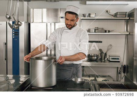 Chef cooking tasty dish in kitchen of restaurant using modern equipment Chef cooking tasty dish in kitchen of restaurant using modern equipment 93972698