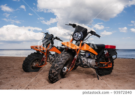 Two custom off-road sports motorcycles are parked on beach outdoors 93972840