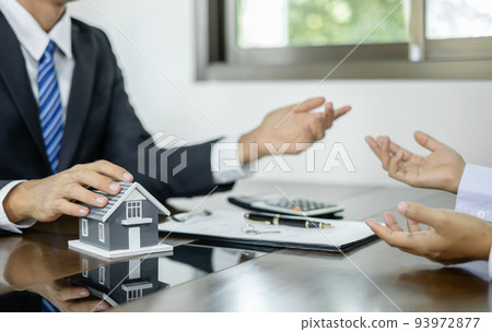 A real estate agent with a House model is talking to clients about buying home insurance. Home insurance concept 93972877