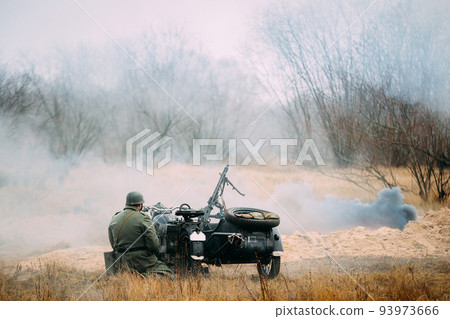 Re-enactor Dressed As World War Ii German Wehrmacht Infantry Soldier Sit Near Old Tricar, Armed Machinegun. Smokescreen. Army Three-wheeled Motorcycle In Autumn Field. Battlefield 93973666