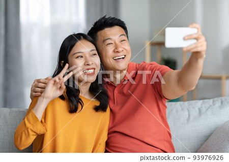 Loving asian couple using cell phone, taking selfie Loving asian couple using cell phone, taking selfie 93976926