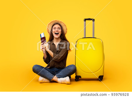 Excited Lady Tourist Holding Tickets Sitting Near Suitcase, Yellow Background Excited Lady Tourist Holding Tickets Sitting Near Suitcase, Yellow Background 93976928