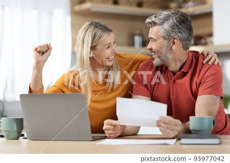Happy emotional spouses reading letter, kitchen interior Happy emotional spouses reading letter, kitchen interior 93977042