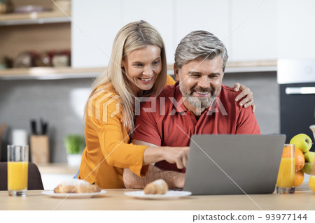 Loving couple enjoying healthy breakfast, using computer, kitchen interior 93977144