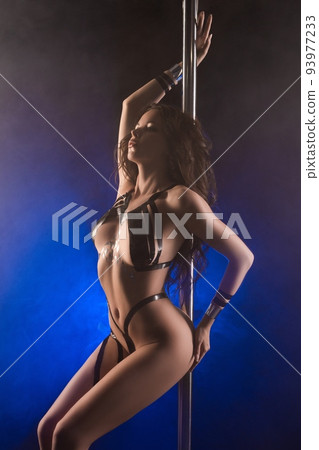 Sensual young woman dancing near pole in studio 93977233