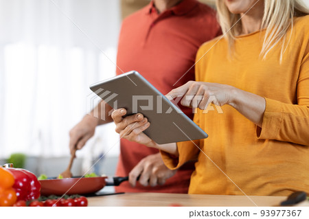 Cropped of couple cooking healthy food, checking recipes online Cropped of couple cooking healthy food, checking recipes online 93977367