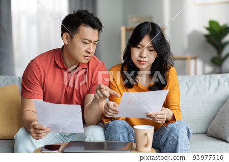 Confused asian spouses checking bills, home interior Confused asian spouses checking bills, home interior 93977516