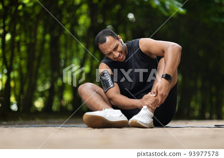 African american athlete in pain touching his ankle 93977578