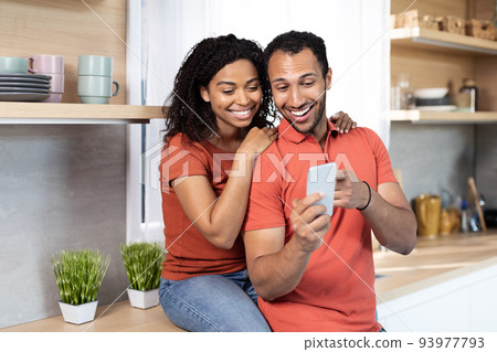 Smiling young african american male and female in same t-shirts have video call on smartphone or watch video Smiling young african american male and female in same t-shirts have video call on smartphone or watch video 93977793