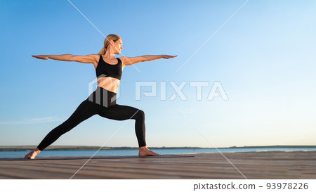 Beautiful Middle Aged Woman Practicing Yoga Outdoors, Standing In Warrior Pose Beautiful Middle Aged Woman Practicing Yoga Outdoors, Standing In Warrior Pose 93978226