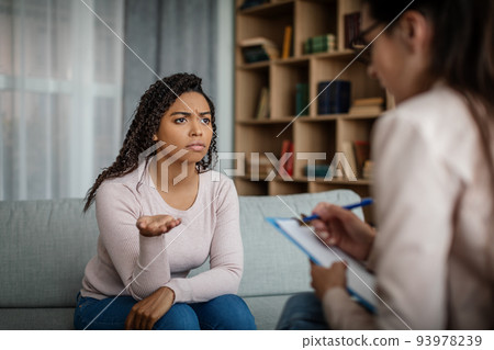Unhappy sad black millennial woman patient talking with european doctor in clinic interior Unhappy sad black millennial woman patient talking with european doctor in clinic interior 93978239