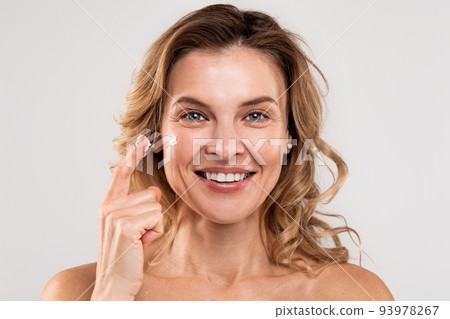 Portrait Of Beautiful Mature Woman Applying Nourishing Cream On Face 93978267