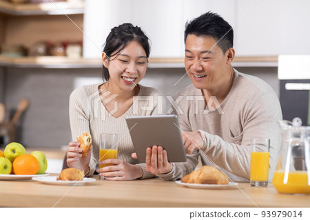 Smiling chinese spouses having breakfast and using tablet Smiling chinese spouses having breakfast and using tablet 93979014