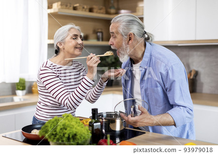 Cheerful senior couple having fun while preparing lunch together in kitchen Cheerful senior couple having fun while preparing lunch together in kitchen 93979018