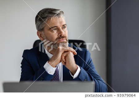 Portrait Of Pensive Middle Aged Businessman In Suit At Workplace In Office 93979064
