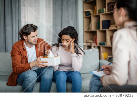 Unhappy caucasian husband calms and support crying black woman on consultation with psychologist Unhappy caucasian husband calms and support crying black woman on consultation with psychologist 93979232