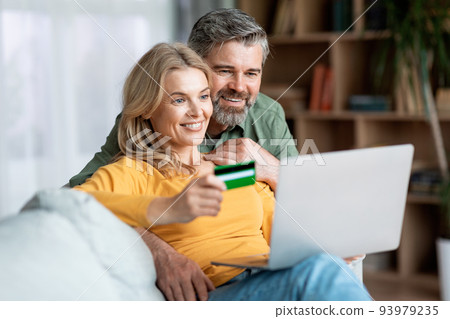E-Commerce Concept. Smiling Middle Aged Spouses With Laptop And Credit Card E-Commerce Concept. Smiling Middle Aged Spouses With Laptop And Credit Card 93979235