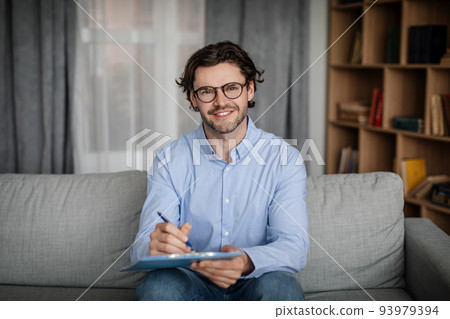 Happy european millennial male doctor in glasses makes notes in clinic interior, empty space 93979394