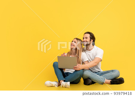 Cheerful surprised millennial caucasian woman and guy sitting on floor with laptop and looking up at empty space Cheerful surprised millennial caucasian woman and guy sitting on floor with laptop and looking up at empty space 93979418