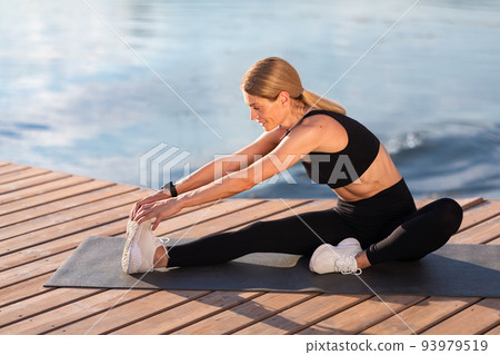 Smiling Athletic Middle Aged Woman Stretching Leg Muscles During Training Outdoors Smiling Athletic Middle Aged Woman Stretching Leg Muscles During Training Outdoors 93979519