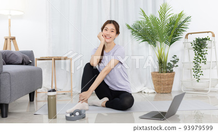 Beautiful Asian woman watching yoga teacher and light exercises in her living room at home, Watch live teaching or VDO on laptop, Dumbbells and a protein shake or bottle of water, Healthy exercise. 93979599