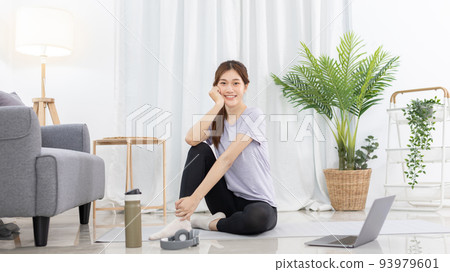 Beautiful Asian woman watching yoga teacher and light exercises in her living room at home, Watch live teaching or VDO on laptop, Dumbbells and a protein shake or bottle of water, Healthy exercise. 93979601