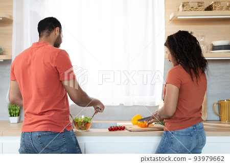 Young african american couple in same t-shirts cooking homemade food together with vegetables Young african american couple in same t-shirts cooking homemade food together with vegetables 93979662