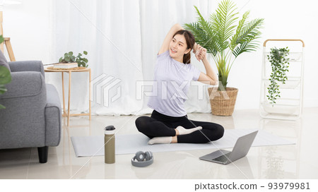 Beautiful Asian woman in sportswear is warming up or doing light exercises in the house with dumbbells and a protein shake or bottle of water and using a laptop at home, Healthy exercise. 93979981