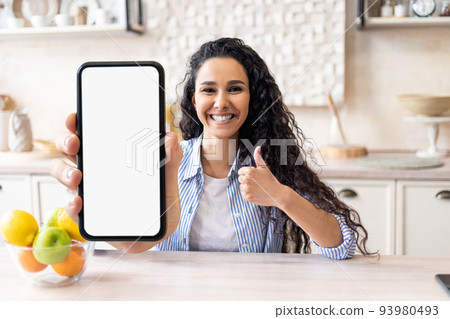 Online Offer. Joyful Young Woman Sitting In Kitchen And Showing Blank Smartphone 93980493