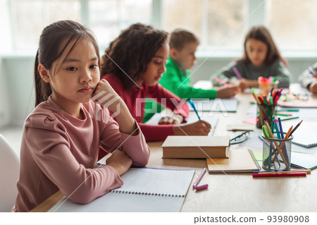Unhappy Asian Schoolgirl Thinking Sitting With Diverse Classmates In Classroom Unhappy Asian Schoolgirl Thinking Sitting With Diverse Classmates In Classroom 93980908